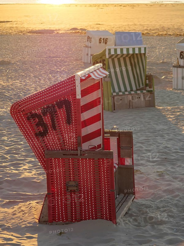 Red and white beach chair on a sandy beach at sunset, sunset on a quiet beach with many colourful beach chairs, warm evening light by the sea, Langeoog, GERMANY