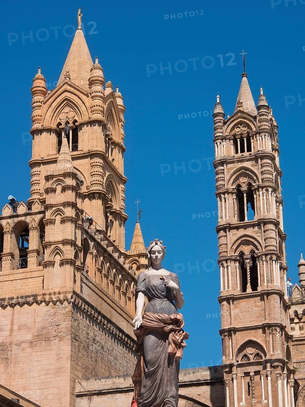 Historic cathedral with detailed towers and a central statue, under a bright blue sky, two red towers in front of a panorama of a large city, Barcelona, Spain, Europe