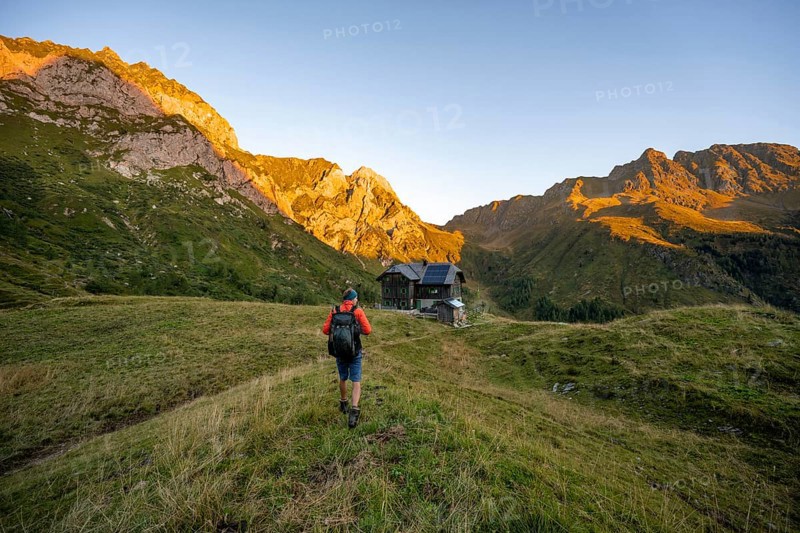 Mountaineers on the way to the Alpine Club hut, Hochweisssteinhaus mountain hut, mountain landscape with green mountain meadows and rocky peaks at sunrise, alpenglow, Carnic High Trail, Carnic Main Ridge, Carnic Alps, Carinthia, Austria, Europe