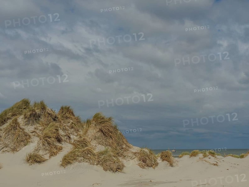 Sand dunes with grass under an overcast sky, dune with dune grass and a boat by the sea, clouds on the beach, nes, ameland, neiderlande