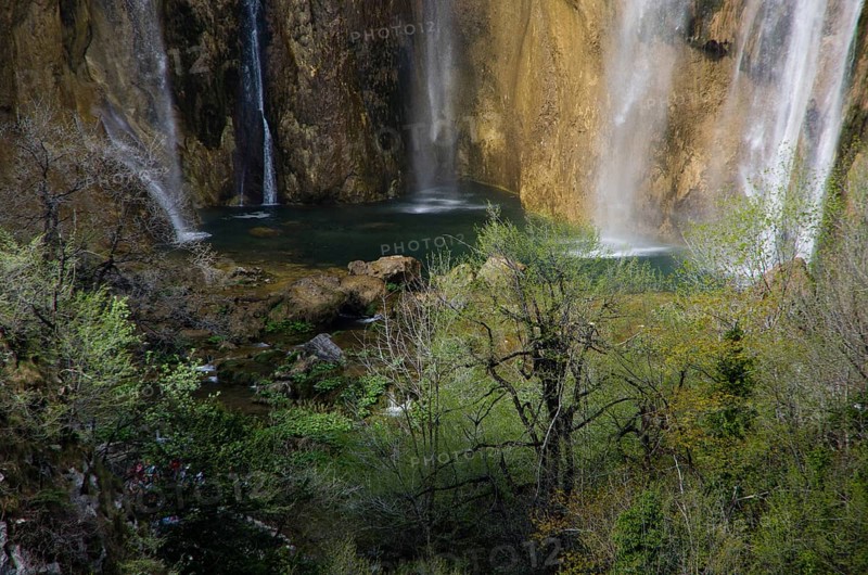A waterfall cascades down between rocks, surrounded by green foliage and trees. Plitvice Lakes National Park, Croatia, Europe