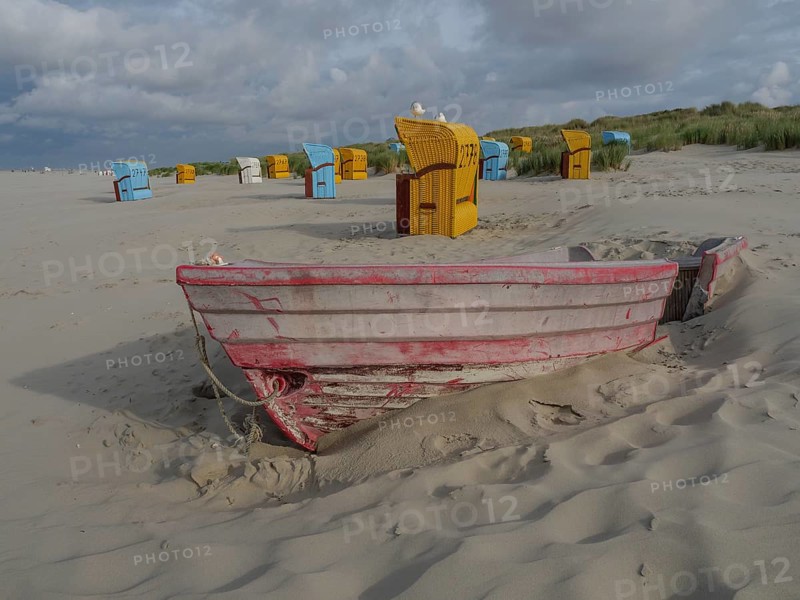 An old boat is buried in the sand, surrounded by colourful beach chairs and cloudy sky, colourful beach chairs on the beach and in the dunes with cloudy sky, red wooden boat and yellow beach chair, Juist, Germany, Europe