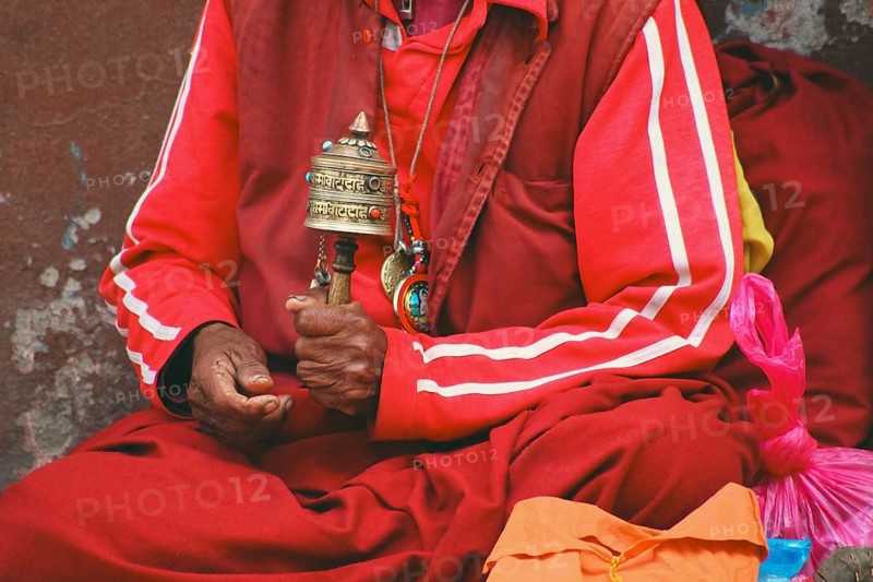 A Tibetan monk in red robes holding a prayer wheel, immersed in spiritual practice