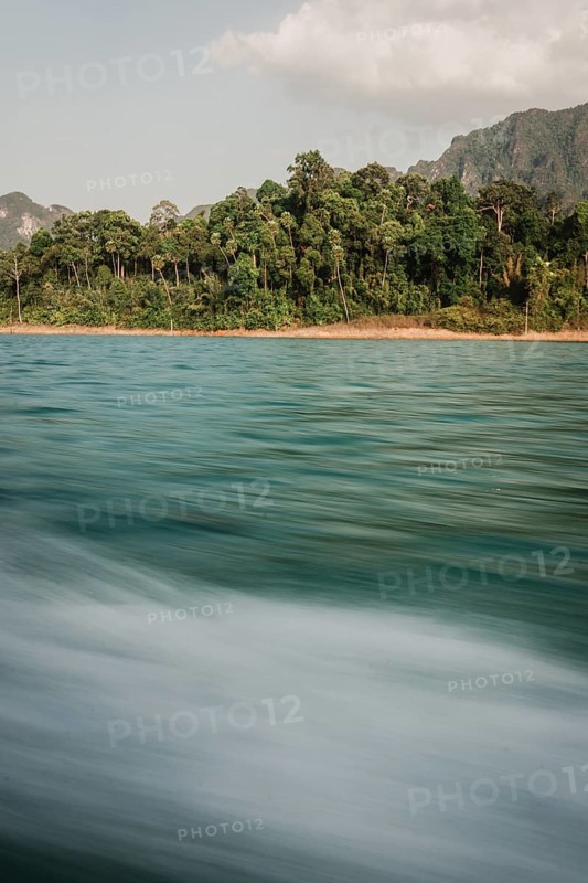 Moving water in front of a picturesque coastline with forest in the background. Khao Sok National Park, Thailand, Asia