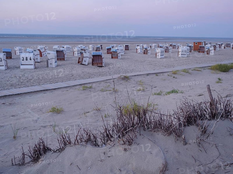 A spacious, quiet beach with white beach chairs and dune grass in the soft light of dusk, setting sun on a beach with beach chairs and clouds in the sky, spiekeroog, germany