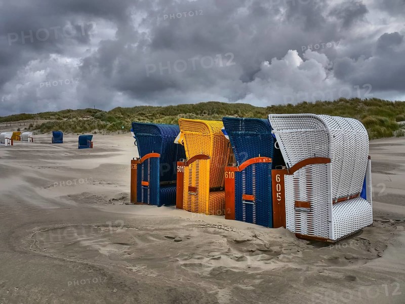 A group of colourful beach chairs on the coast in unstable weather, colourful beach chairs on the beach and in the dunes under cloudy skies by the sea, Juist, Germany, Europe