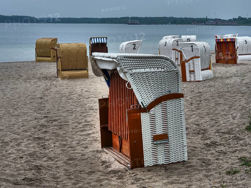 A quiet beach with several beach chairs and a stone quay in the background under a cloudy sky, beach chairs on a quiet sandy beach by the sea, clouds over the sea, Eckernfoerde, germany