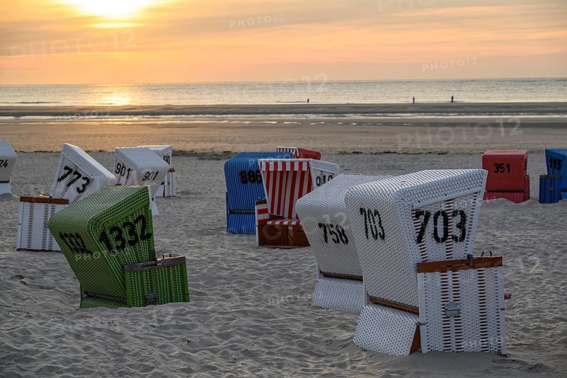 White, red and green beach chairs on a sandy beach at sunset, many colourful beach chairs on a warm summer evening by the sea, langeoog, germany