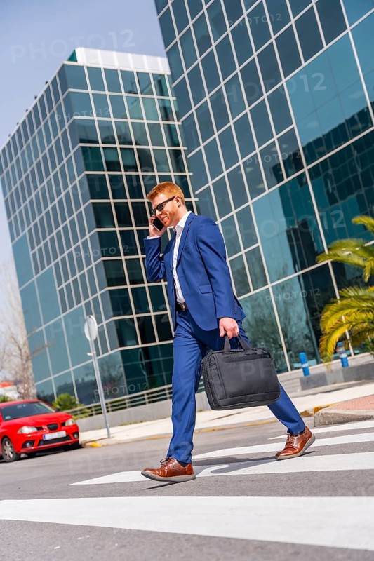 Vertical full length photo of a cool businessman talking to the mobile walking along the city
