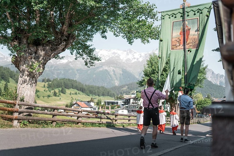 People in traditional traditional costume carry a banner through an Alpine village in sunny weather. Nauders, Austria, Europe