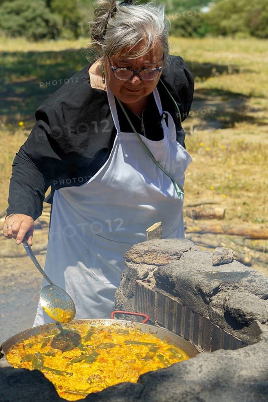 Woman chef in white apron cooking a typical Spanish paella over a wood fire in a stone kitchen in the countryside