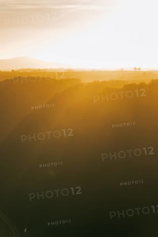The sun shines through a gap in the clouds over a field with trees. Niederfell, Germany, Europe