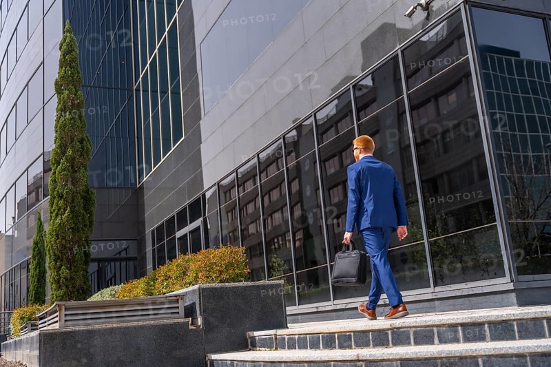 Full length rear view of a businessman with laptop bag and suit walking along a financial district