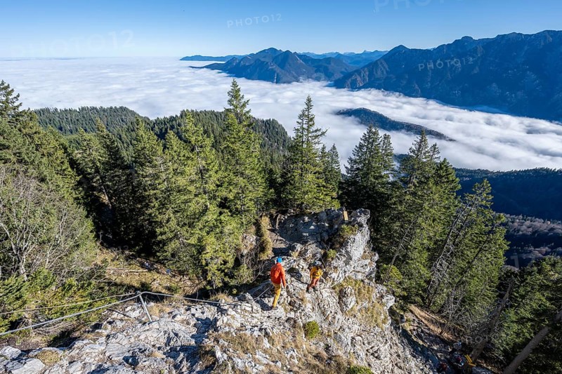 Two friends, mountaineers climbing the via ferrata to the rocky summit of the Ettaler Manndl, view over mountain landscape and sea of clouds, high fog in the valley, Ammergau Alps, Bavaria, Germany, Europe