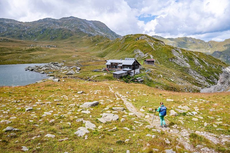 Hiker on hiking trail to Obstanserseehuette, mountain lake Obstansersee between green mountain meadows, Carnic Main Ridge, Carnic High Trail, Carnic Alps, Carinthia, Austria, Europe