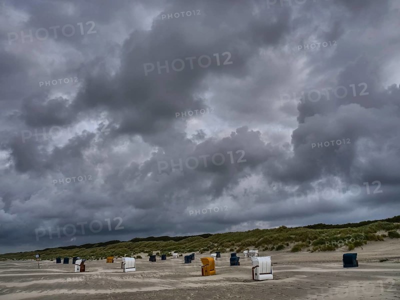 Dark clouds towering over a grey beach with scattered beach chairs, colourful beach chairs on the beach and in the dunes under an overcast sky by the sea, Juist, Germany, Europe