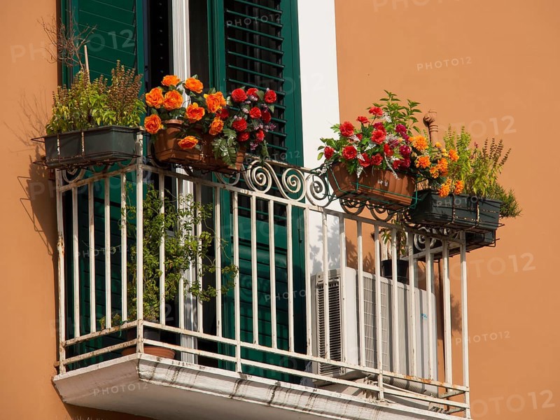 A small balcony with flowers in pots, green shutters and an air conditioner in front of an orange-coloured wall, small balconies decorated with flowers on old houses, bari, italy
