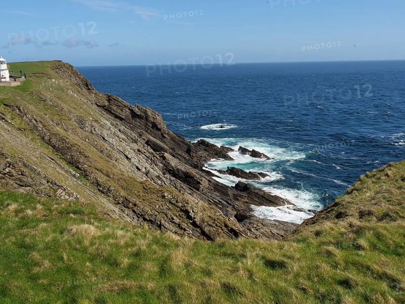 Steep cliffs with green grass and views of the azure sea and undulating coastline under a blue sky, green meadows on a deep blue sea and a rocky coastline with individual houses, lerwick, shetland, Scotland, United Kingdom, Europe