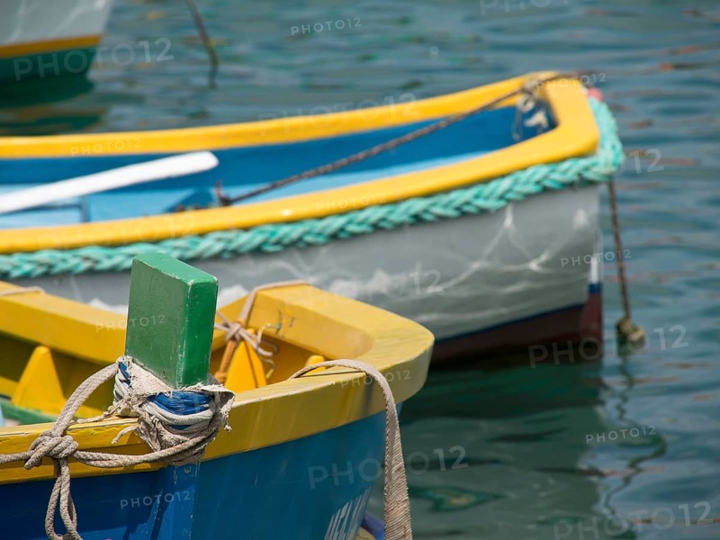 Close-up of a part of a yellow and blue fishing boat in the water, many colourful fishing boats in a harbour in the Mediterranean Sea, Marsaxlokk, malta