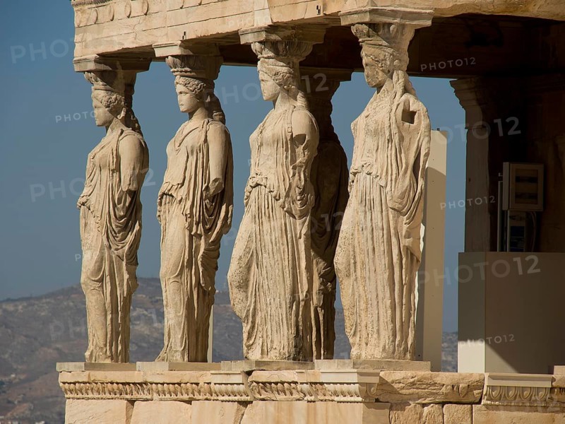 Statues of caryatids replacing columns on the Acropolis, historical columns and ruins on an ancient site against a blue sky, Athens, Greece, Europe