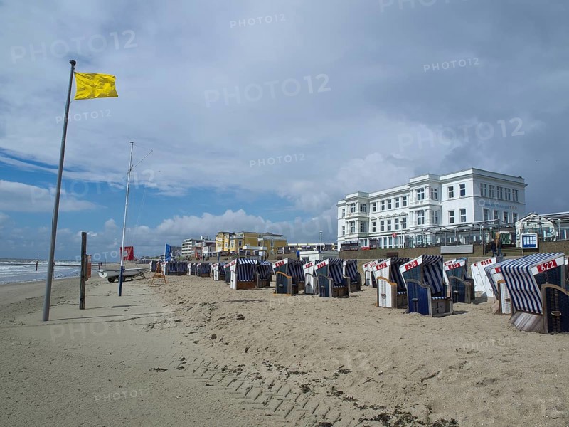 View of beach chairs on the beach in front of buildings and a yellow flag under a cloudy sky, blue and white striped beach chairs on the seashore, Norderney, Germany, Europe