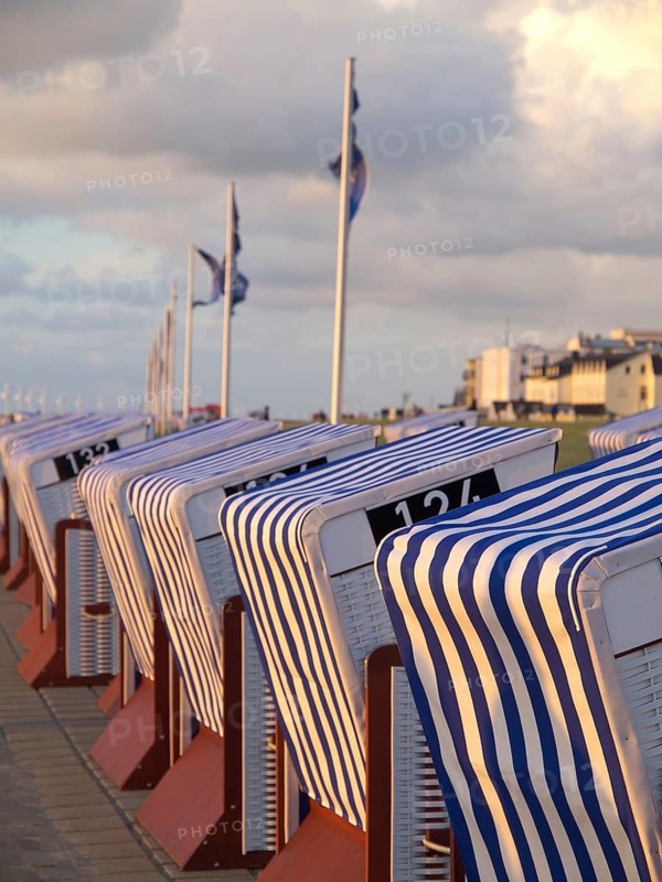 Row of striped beach chairs at sunset by the sea, with buildings and clouds in the background, blue and white striped beach chairs on the seashore, Norderney, Germany, Europe