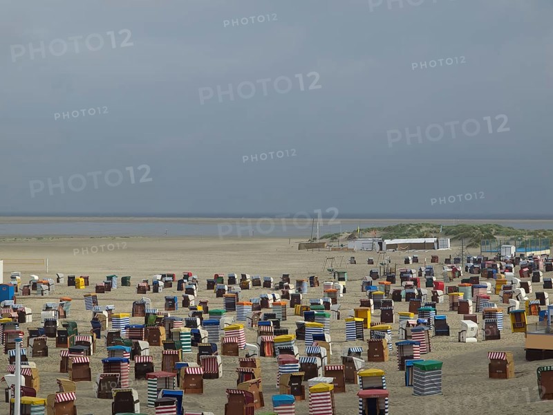 Numerous colourful beach chairs are located in large numbers on the empty beach with a wide view of the sea, beach chairs and beach tents by the sea under a cloudy sky, boardwalk in the sand, Borkum, germany