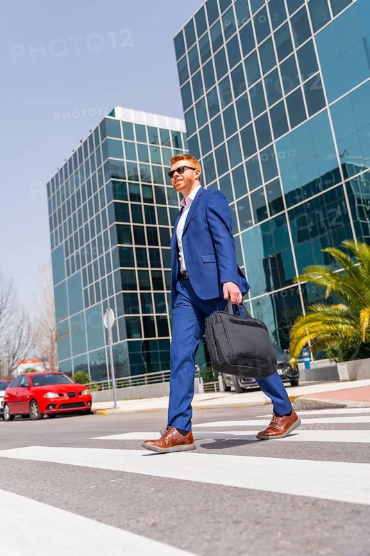 Vertical full length photo with low angle view of an elegant cool businessman crossing the street