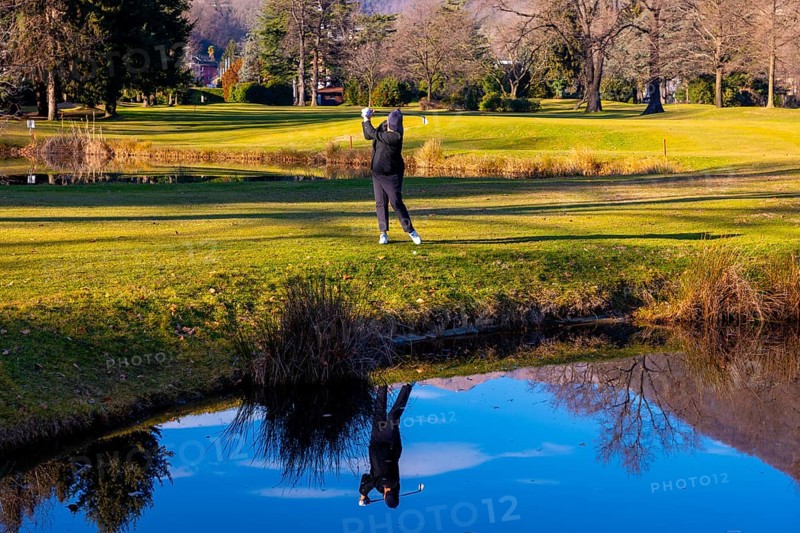 Female Golfer Reflected in a Water Pond and Hitting the Golf Ball on Fairway on Golf Course in a Sunny Day in Switzerland