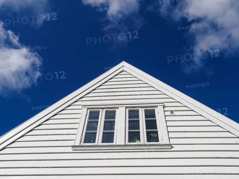 White wooden house with a window in a triangular gable in front of a bright blue sky with few clouds, White wooden houses in front of a blue sky, Stavanger, norway