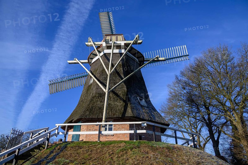 A historic windmill on a hill under a clear blue sky, surrounded by trees, Old windmill with a fence and a tree against a blue sky, empty, Germany, Europe