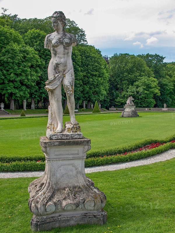 Weathered statue in a well-kept park with green lawns and surrounded by trees, park with green hedges, small paths and old statues, nordkirchen, germany