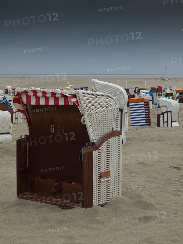 A single beach chair stands on a deserted beach under a cloudy sky, beach chairs and beach tents by the sea under a cloudy sky, boardwalk in the sand, Borkum, germany