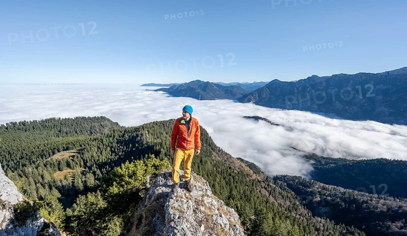 Mountaineer on the rocky summit of the Ettaler Manndl, view over mountain landscape and sea of clouds, high fog in the valley, Ammergau Alps, Bavaria, Germany, Europe