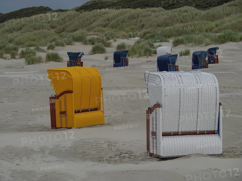 A yellow and a white beach chair are standing on the beach, with dunes and several other baskets in the background, colourful beach chairs on the beach and in the dunes with overcast sky at the sea, Juist, Germany, Europe