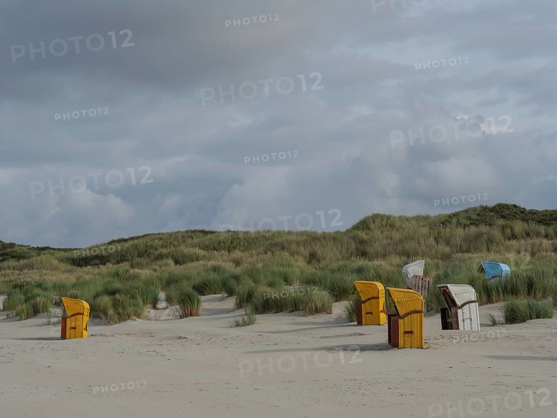 A wide dune landscape with scattered beach chairs under a cloudy sky, colourful beach chairs on the beach and in the dunes under an overcast sky, red wooden boat and yellow beach chair, Juist, Germany, Europe