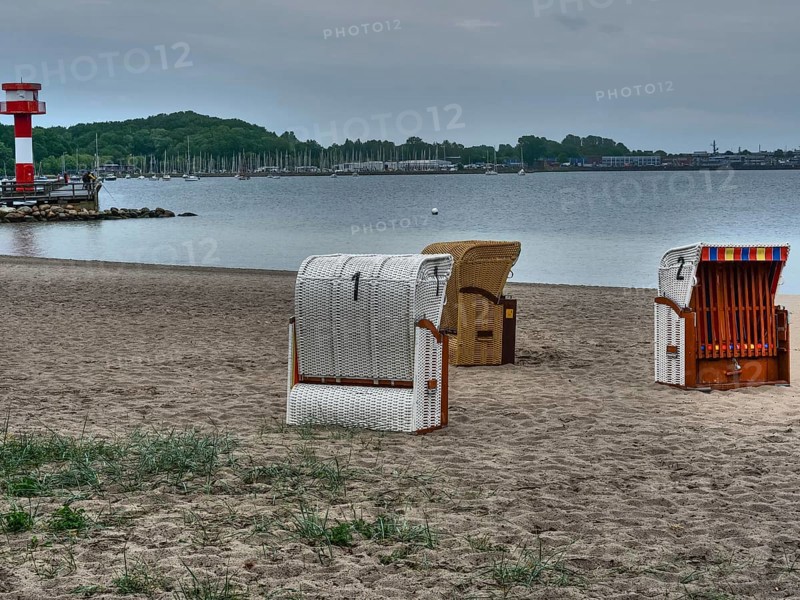 A cloudy day on the beach with a lighthouse in the background and several beach chairs on the sand, beach chairs on a quiet sandy beach by the sea, clouds over the sea, Eckernfoerde, germany
