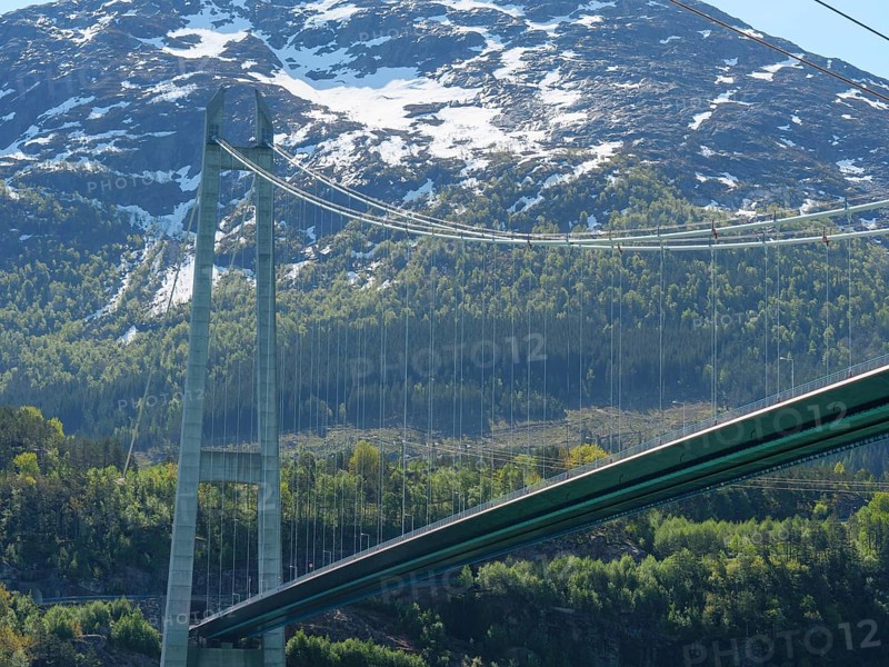 Bridge against a backdrop of snow-capped mountains and green forests under a clear blue sky, bridge in a fjord with snow-capped mountains and green trees, greenish shimmering water, eidfjord, Norway, Europe
