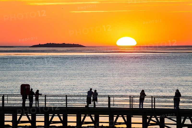 Silhouettes of several people on the pier free canal, jetty, couples and individuals watch the picturesque, golden, breathtakingly beautiful sunset over the sea, island Langluetjen II on the horizon, sun half sunk, orange glowing cloudless sky, wide sea in soft colours, mouth of the Weser into the North Sea, Outer Weser, Bremerhaven, Land Bremen, Germany, Europe