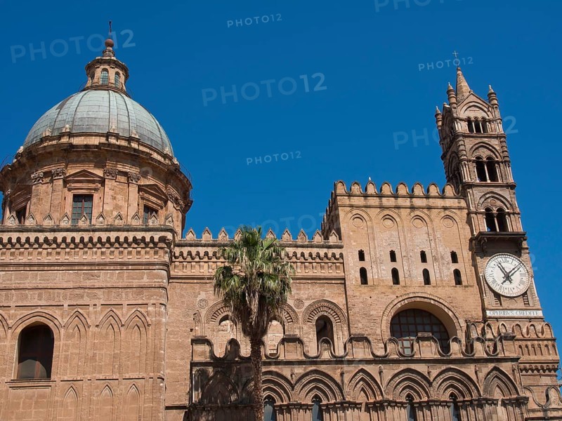 Side view of a historic cathedral with a striking dome and a clock on the tower, against a blue sky, two red towers in front of a panorama of a large city, Barcelona, Spain, Europe