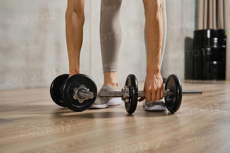 Closeup view of muscular female arms lifting dumbbells from the floor