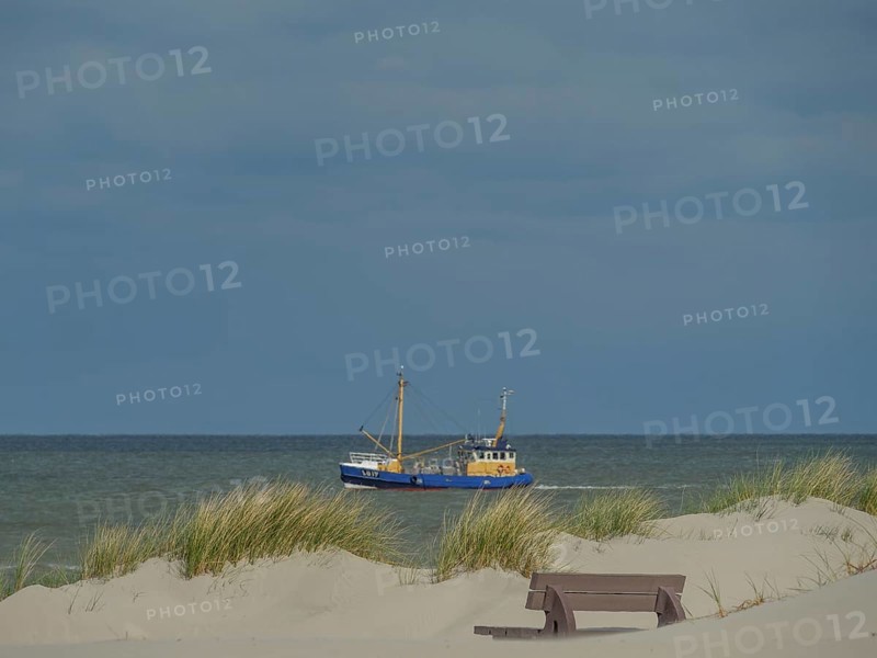 A fishing boat on the sea, in the foreground dunes and a bench under a cloudy sky, dunes on an island with a blue boat and a bench, clouds and sand by the sea, nees, ameland, the netherlands