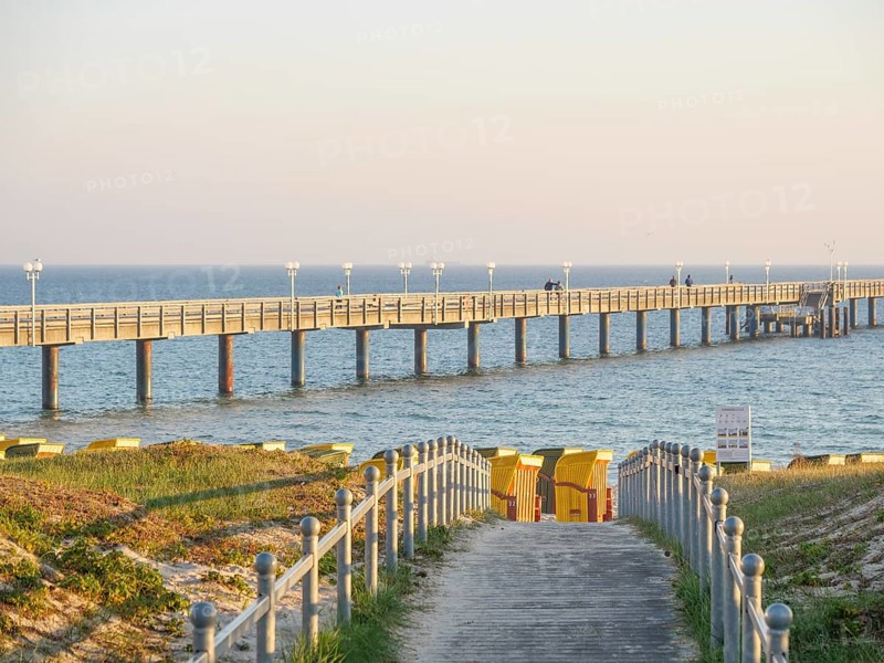 A long jetty leads into the sea, next to it beach chairs and a yellow sky at sunset, beach chairs in the morning light under a blue sky by the sea, pier in the sea, Binz, Germany, Europe