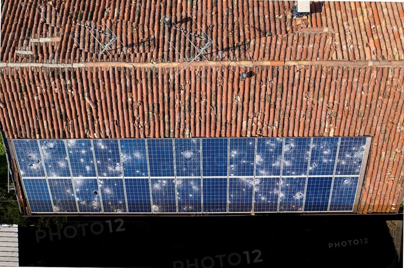Direct overhead view of a roof with terracotta tiles and damaged solar panels casting shadows