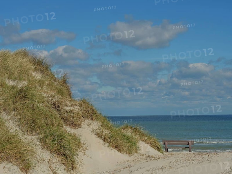 Sand dunes with grass, behind them the sea and a bench, above them a cloudy sky, dunes on an island with a blue boat and a bench, clouds and sand by the sea, nees, ameland, the netherlands