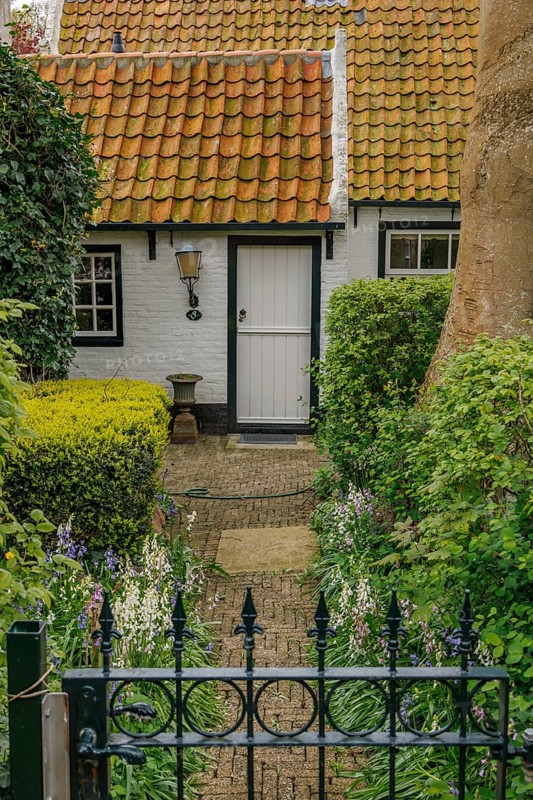 Small cosy house with red tiled roof and well-kept garden, old houses with green gardens in a small village, nes, ameland, the netherlands