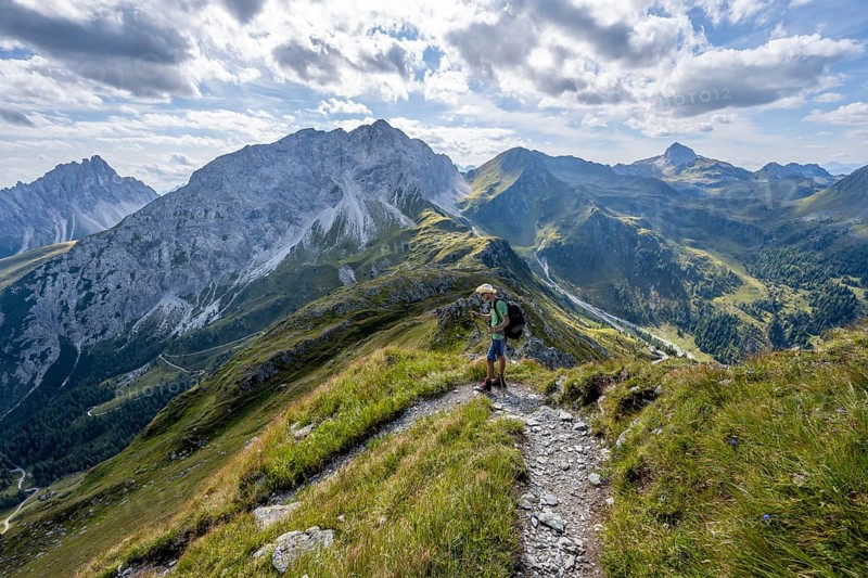 Mountaineer on a hiking trail on a grassy mountain ridge, idyllic mountain landscape with green mountain meadows, descent from Baerenbadegg, rocky summit Porze in the background, Carnic High Trail, Carnic Main Ridge, Carnic Alps, Carinthia, Austria, Europe