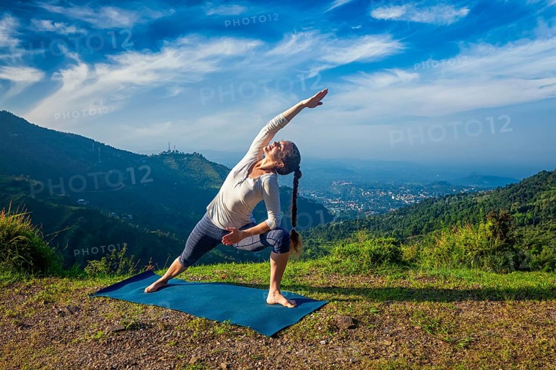 Woman practices yoga asana Utthita Parsvakonasana, extended side angle pose outdoors in mountains in the morning