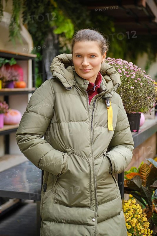 Cheerful woman stands at a display case with potted flowers at autumn flower fair
