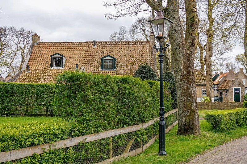 Cosy house in a village, surrounded by green hedges and lanterns, a road leads past, dune and footpaths on the Wadden Sea, clouds in the sky, nes, ameland, the netherlands